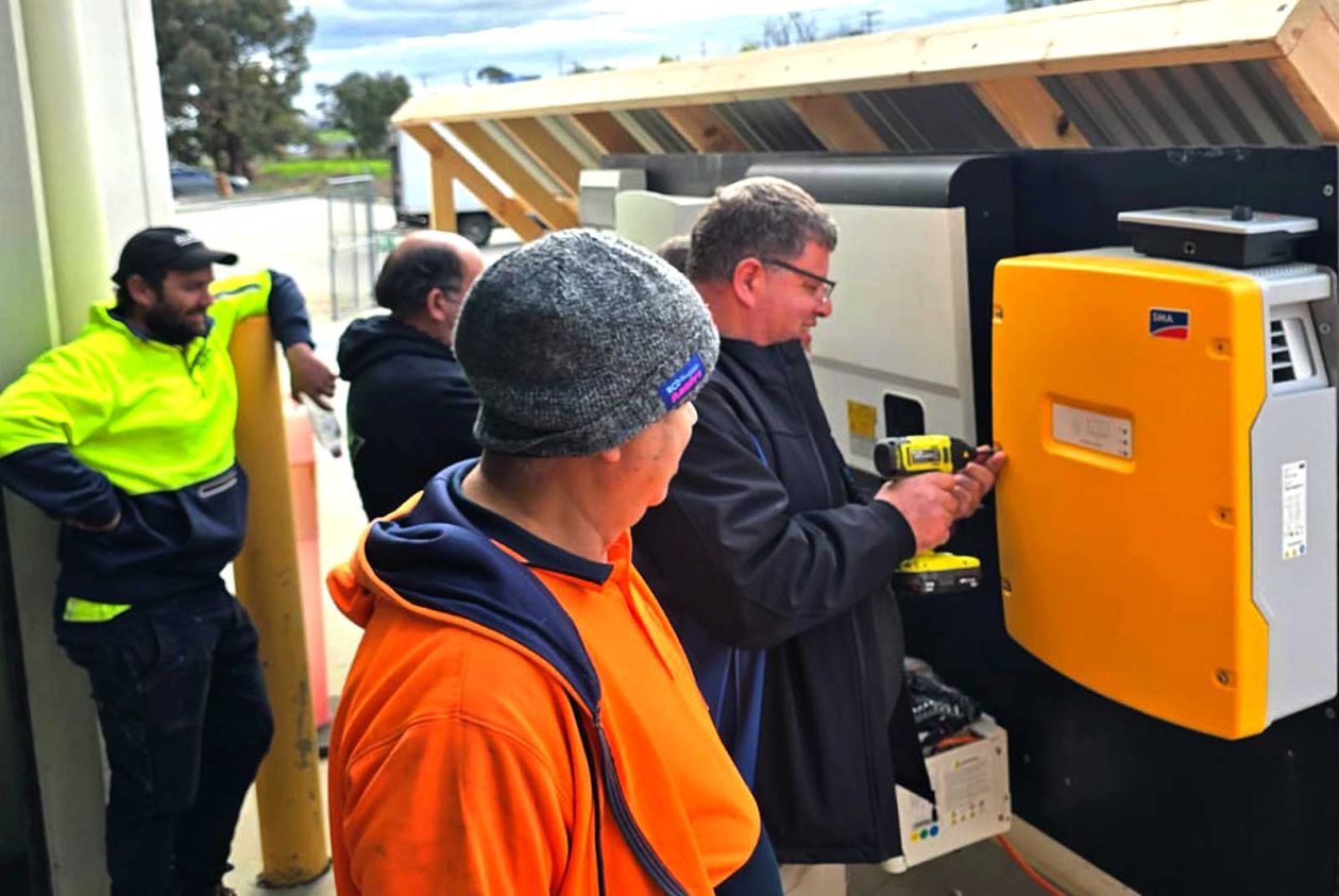 Group of students observing a trainer demonstrating how to install and work with a solar inverter during a hands-on class.