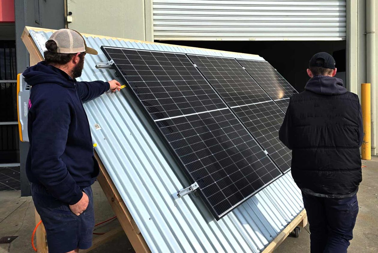 Two students practising solar panel installation on an outdoor training rig